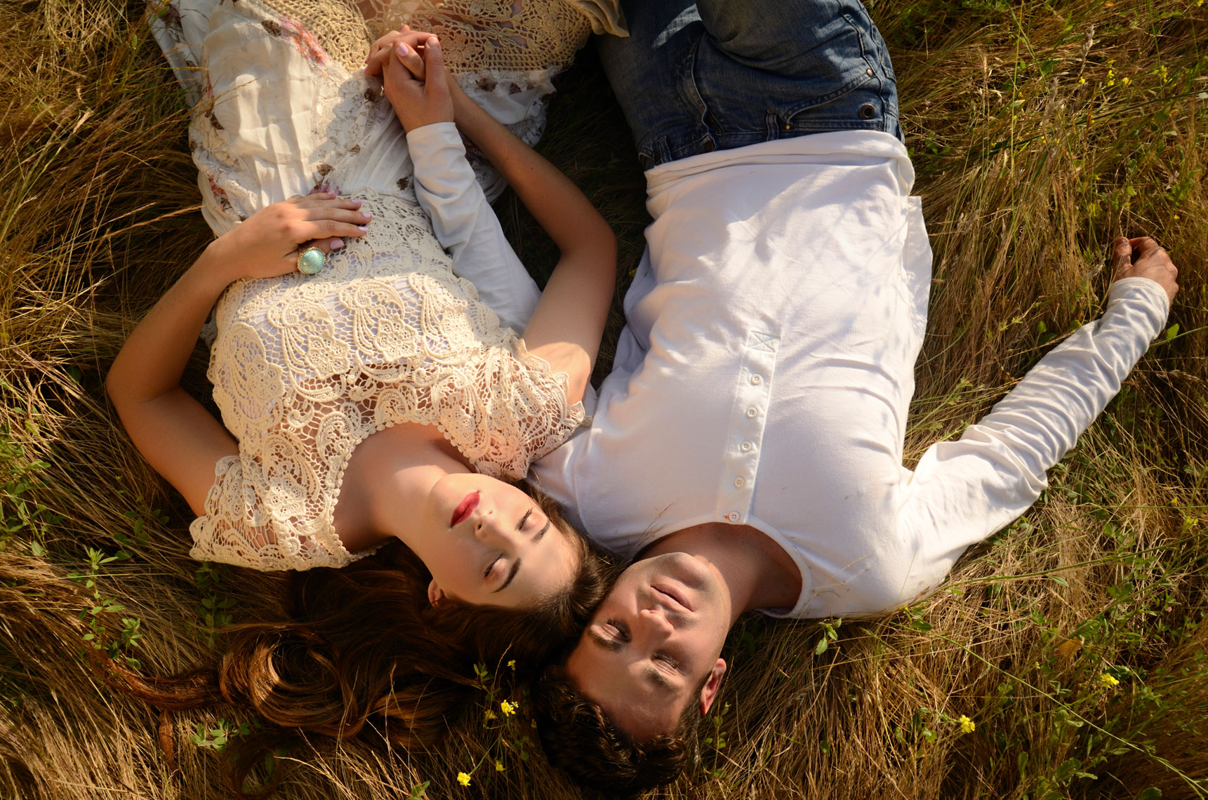 young-romantic-couple-holding-hands-sleeping-in-overgrown-grassy-field-by-lifestyle-photographer-Joe-Atlas.